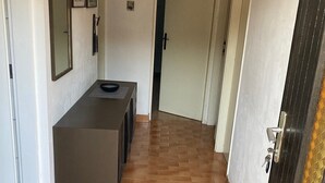 Un pasillo con suelo de baldosas, un mostrador de recepción, un perchero y una puerta con un cartel de bienvenida.
