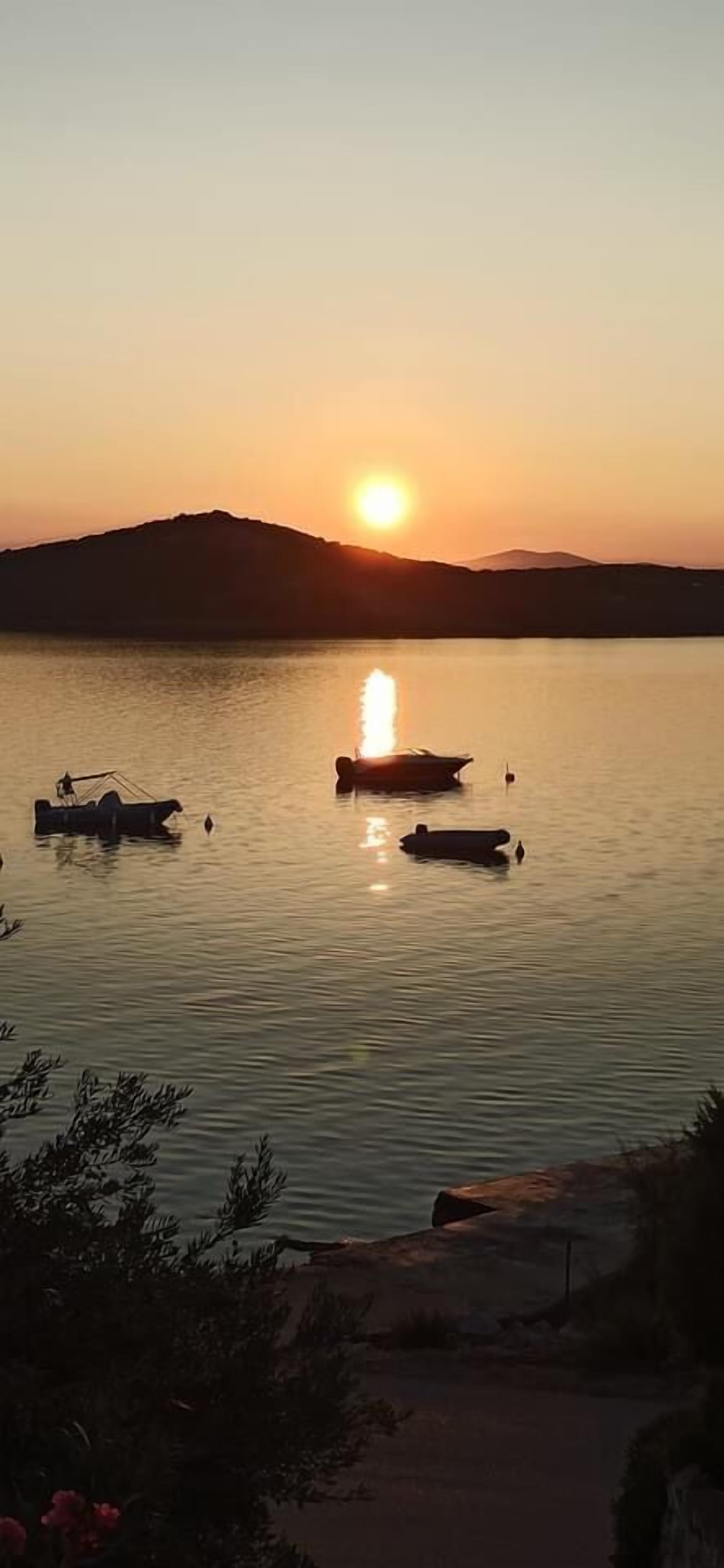 A sunset over a calm body of water with boats and a distant mountain.