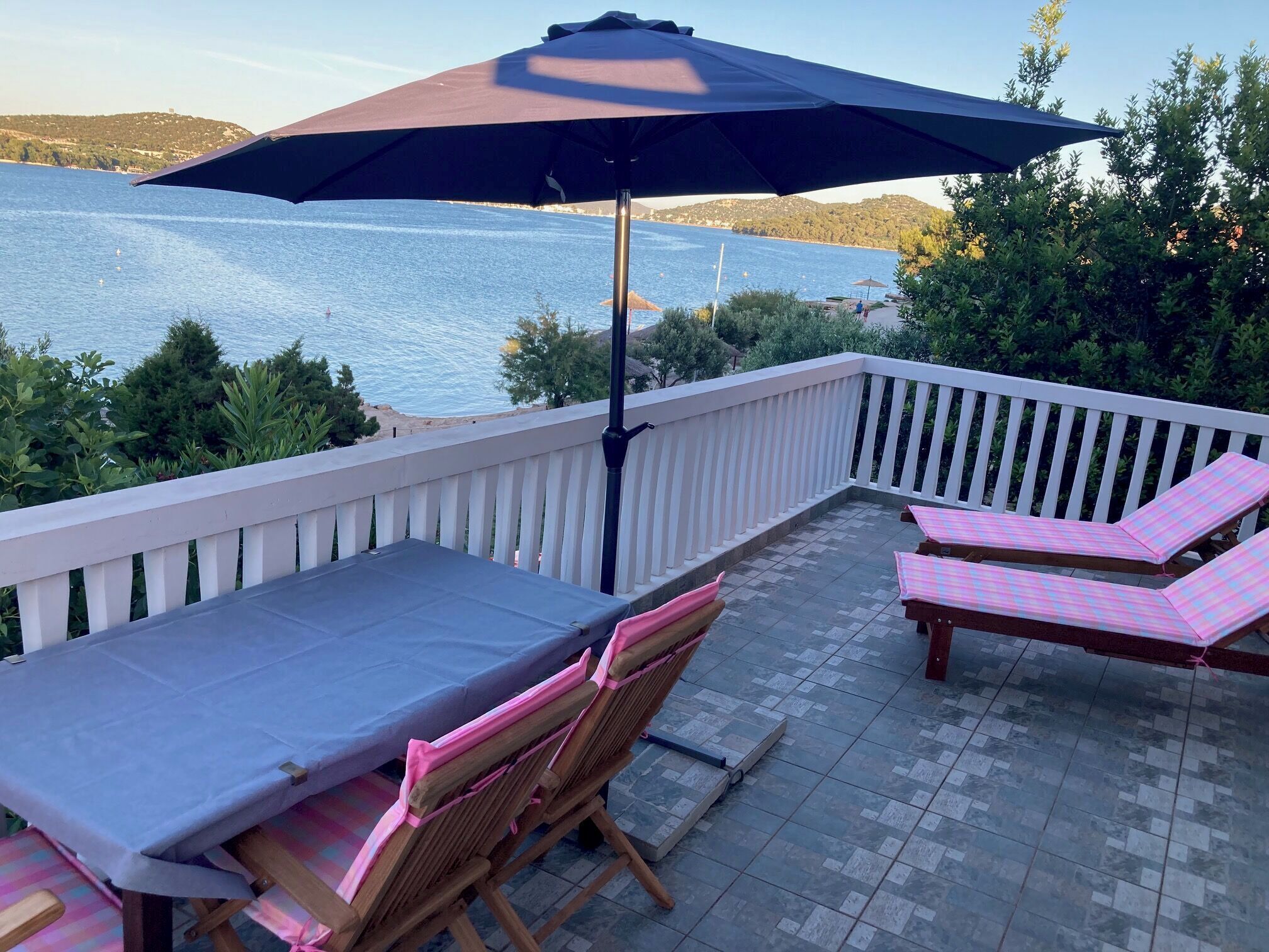 A terrace with a table and chairs, an umbrella, and a view of the sea.