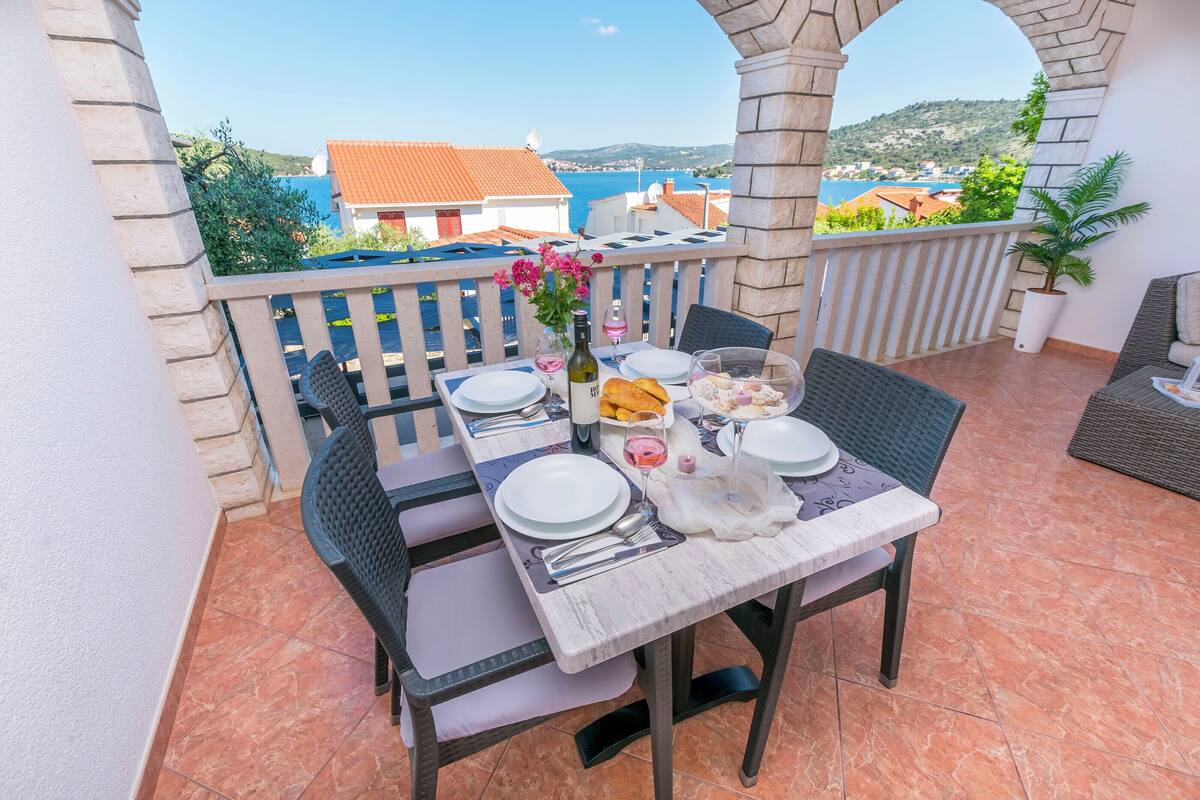 A terrace with a table set for dining, overlooking a scenic view of buildings and a body of water.