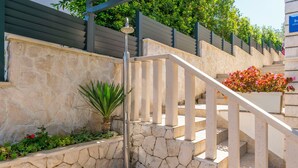 Un escalier en pierre avec une rampe métallique, entouré de verdure et délimité par une clôture en métal.