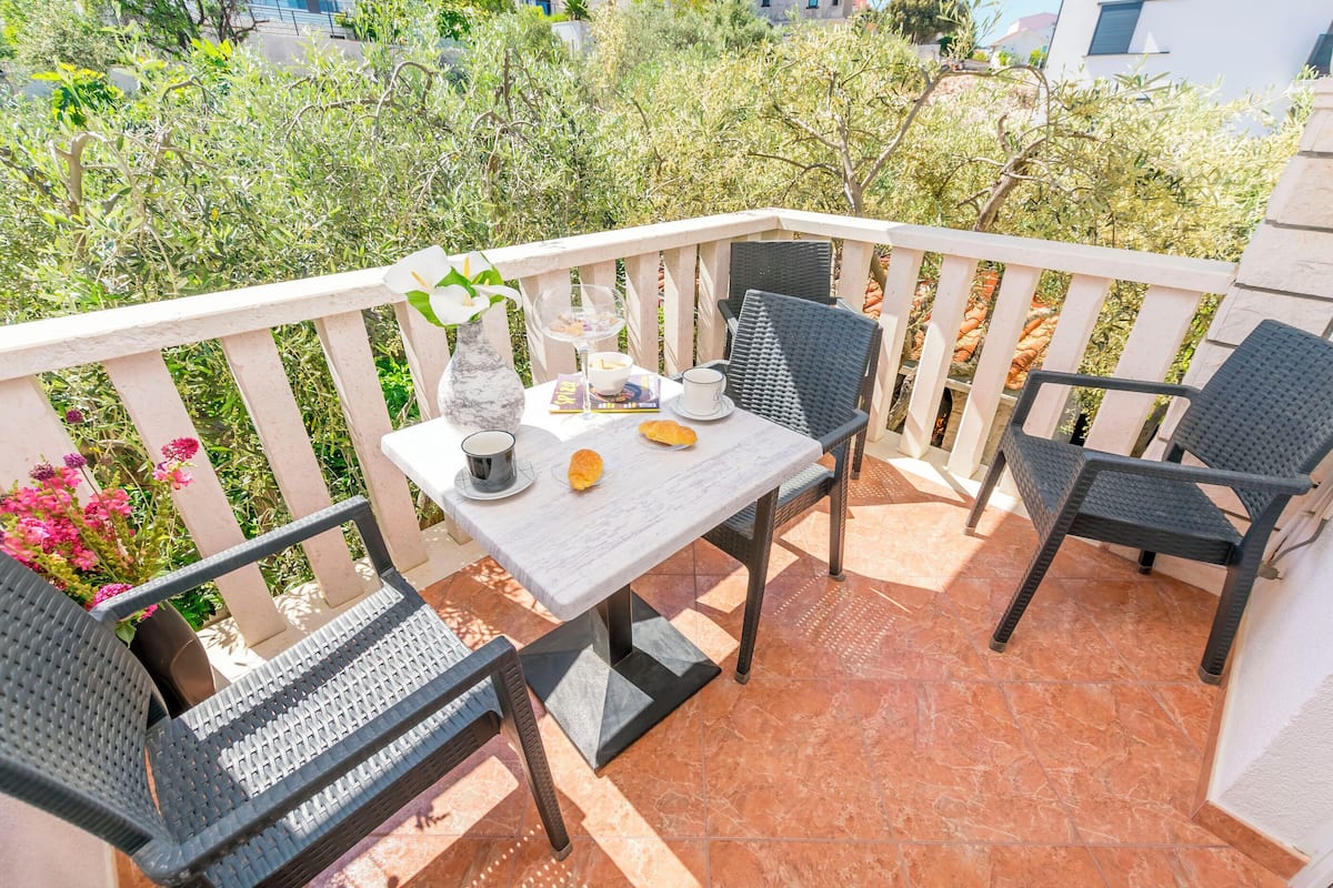 A balcony with a table set for two, featuring a vase with flowers, a book, a cup, and a plate with food.