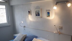 Een slaapkamer met een bed, kussens, een nachtkastje, een raam en wandlampen.