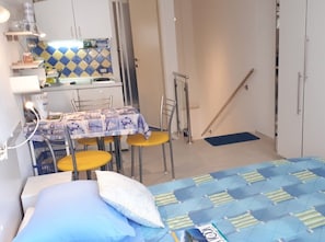 Une chambre compacte comprenant un lit, une petite table avec des chaises, un coin cuisine et une salle de bain.