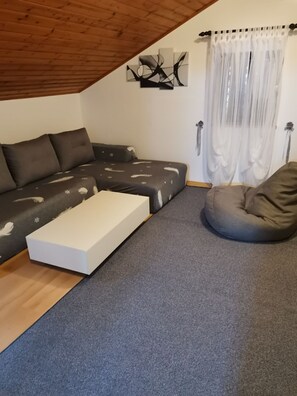 A modern living room with a sectional sofa, a bean bag, a white coffee table, and a ceiling with exposed wooden beams. - Apartment Vanja (Mali Losinj)