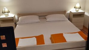 Ein ordentlich bezogenes Bett mit weißer und orangefarbener Bettwäsche, zwei Nachttischlampen und ein kleiner Tisch in einem Zimmer mit Holzboden und weißen Wänden.