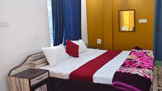 Una camera d'albergo con un letto, un comodino, uno specchio e una finestra con tende.