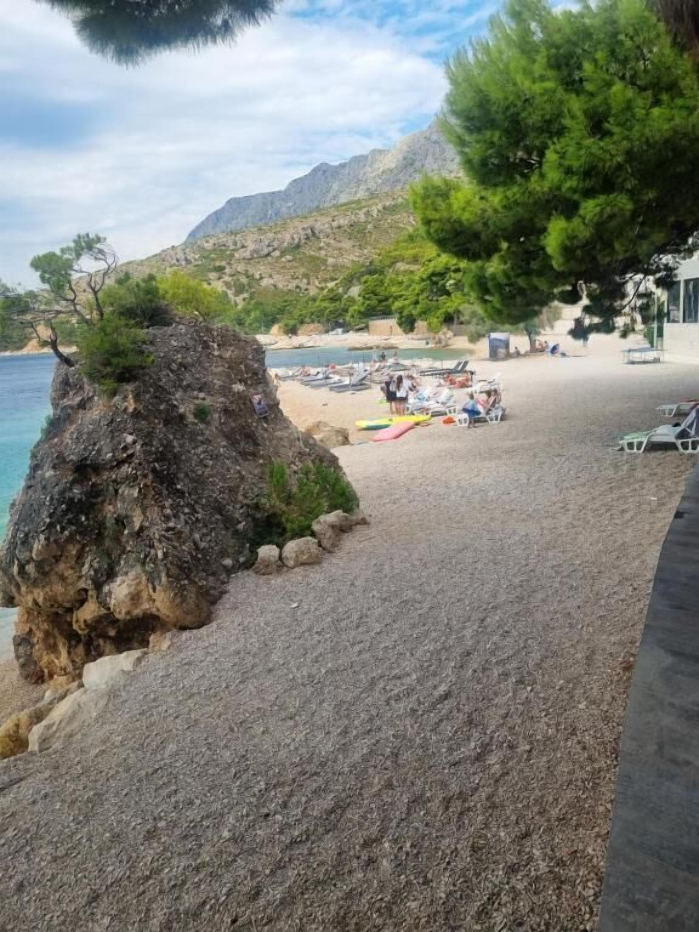 A beach with pebbles, a rock formation, and a few people.