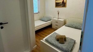 Ein Schlafzimmer mit einem Einzelbett, einem Nachttisch, einer kleinen Kommode, einem Fenster mit Jalousien und einem Bild an der Wand.