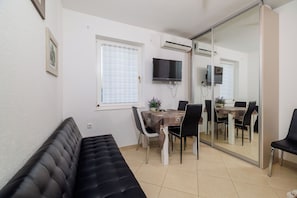 Ein kompakter Wohnbereich mit einer Couch, einem Esstisch mit Stühlen, einem an der Wand befestigten Fernseher und einer Schiebetür aus Glas zu einem anderen Raum.