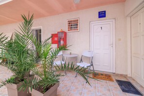 A hotel entrance with a tiled floor, a potted plant, a red mailbox, a small table with chairs, and a door marked with the number 1. - Apartment Roli (Crikvenica)