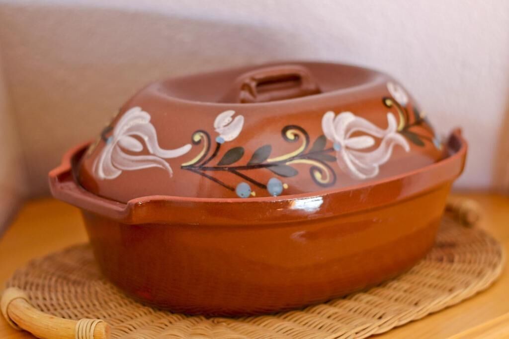 A terracotta pot with a lid, decorated with floral patterns, placed on a woven mat.