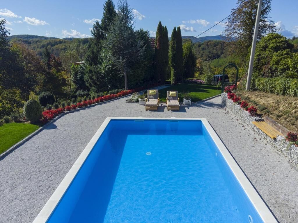 Ein rechteckiger Pool mit Kiesbereich, Rasenfläche und einer Reihe roter Blüten.