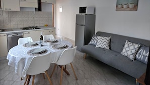A compact kitchen with a dining table set for four, a grey sofa, and a refrigerator. - Apartments Sea and Pine (Jelsa)