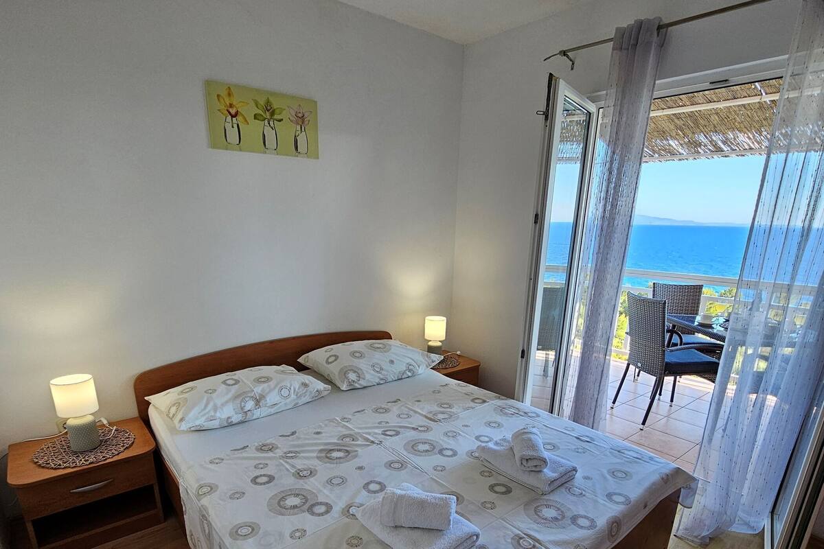 A bedroom with a bed, bedside tables, a nightstand, a painting, and a view of the sea.