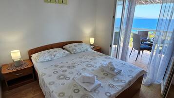 Quarto com cama, mesas de cabeceira, um criado-mudo, um quadro e vista para o mar.