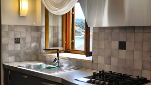A modern kitchen with a built-in gas stove, a stainless steel sink, and a window with a view of a pool and mountains. - House Nonina Kuca (Rab)