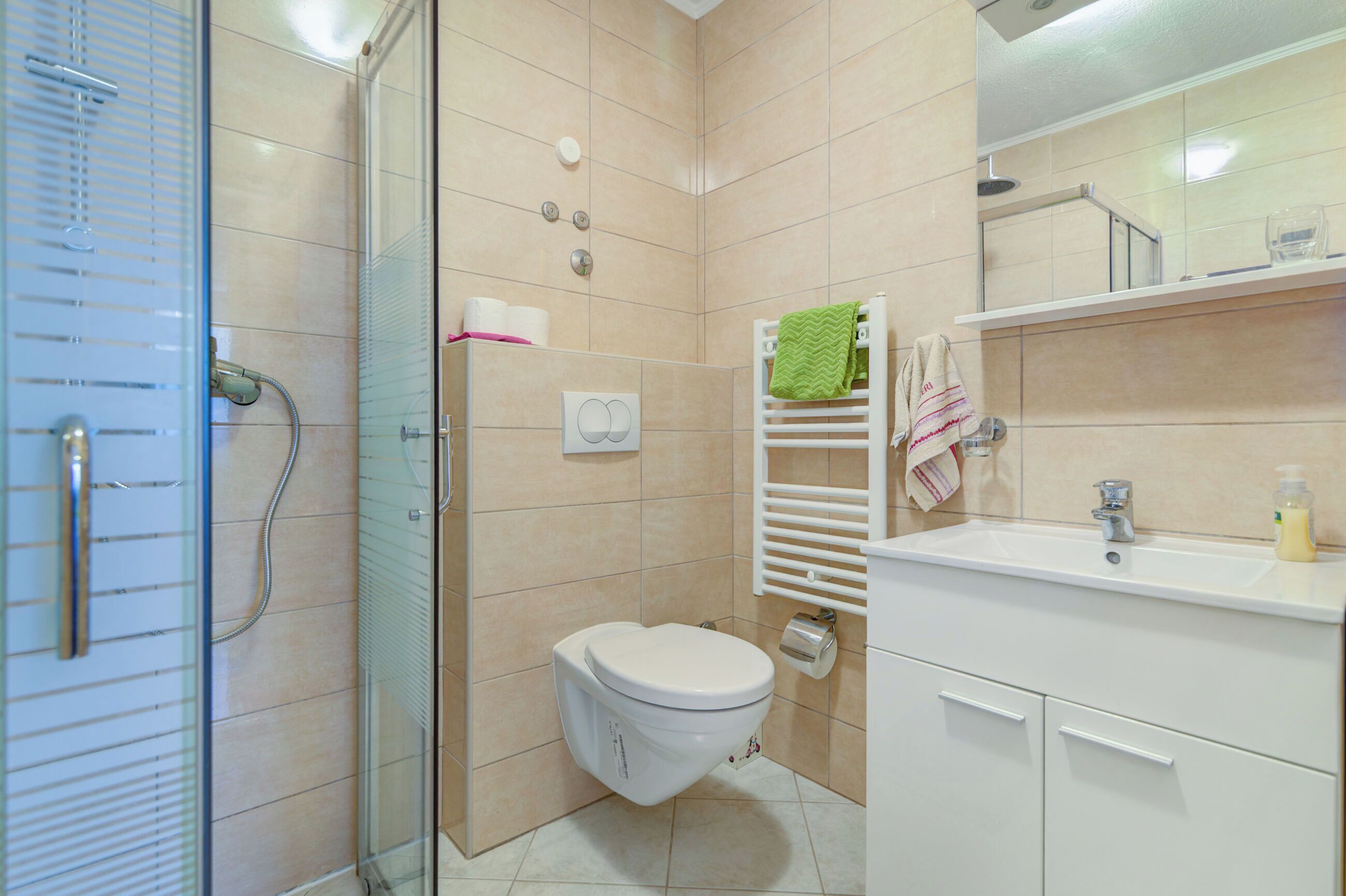 Un bagno moderno con box doccia in vetro, un water, un lavandino e uno specchio.