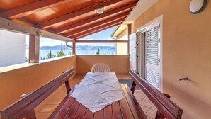Ein Balkon mit Holztisch und -stühlen, Blick auf das Meer und einem weißen Deckenventilator.