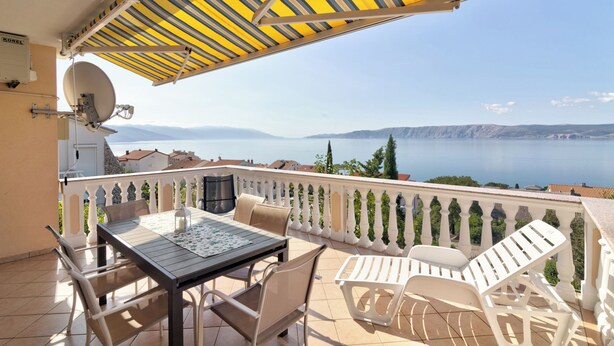Ein Balkon mit Tisch und Stühlen, einer Satellitenschüssel und Blick auf das Meer und die Berge.