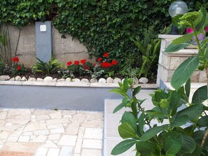 A garden with a stone pathway, red flowers, and a wall with ivy. - Apartment Apartment Yellow (Baska Voda)