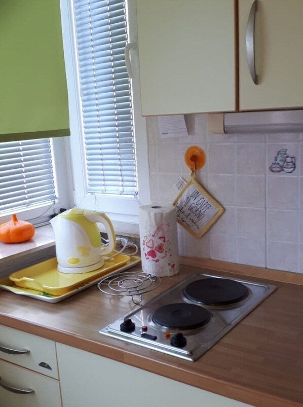 A kitchen with a stove, a kettle, and a window with blinds. - Apartment Apartment Yellow (Baska Voda)