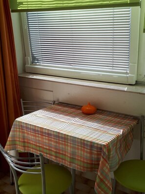 A small dining area with a table covered by a plaid tablecloth, two green chairs, and a window with blinds. - Apartment Apartment Yellow (Baska Voda)