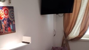 Een woonkamer met een paarse bank, een aan de muur bevestigde televisie en een raam met gordijnen.