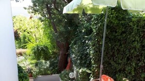 Een terras met een ronde tafel en vier stoelen, omringd door een vloer van stenen tegels en een groene parasol.
