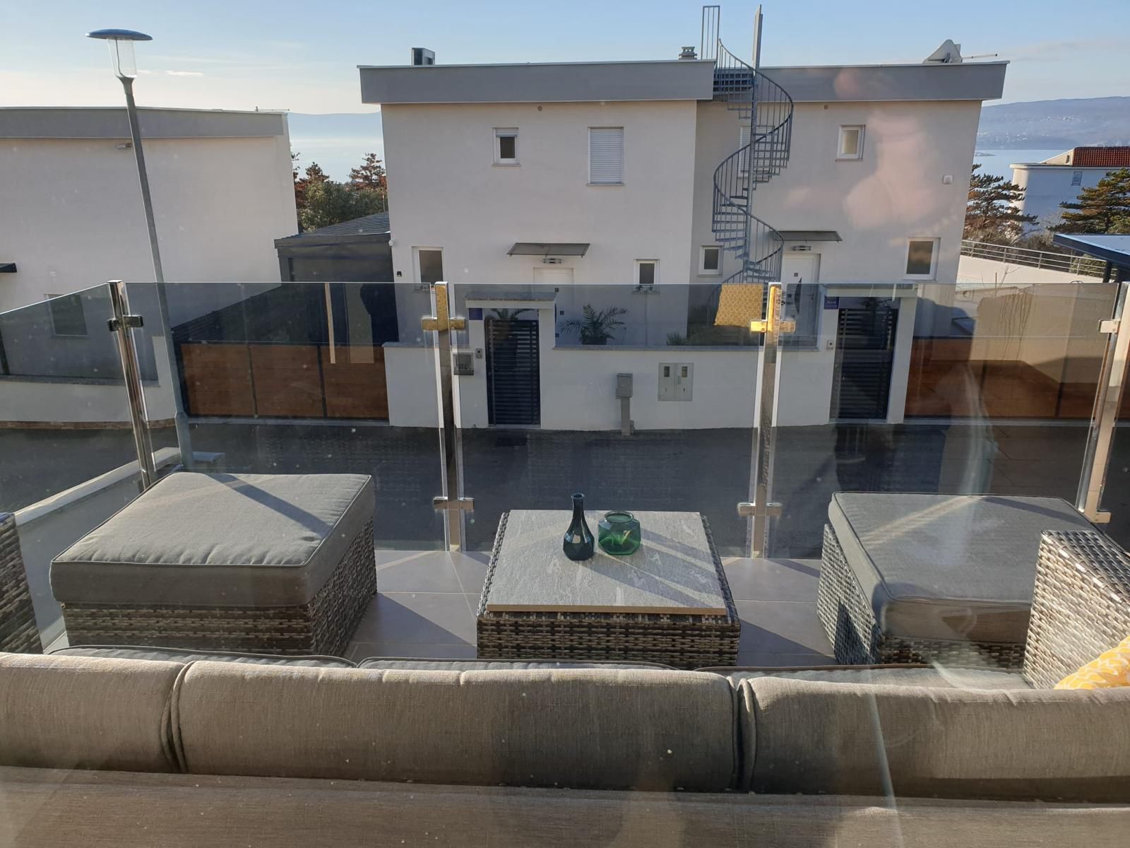 Eine Dachterrasse mit Außenbestuhlung, einer Wendeltreppe und Blick auf ein Gebäude mit weißer Fassade.