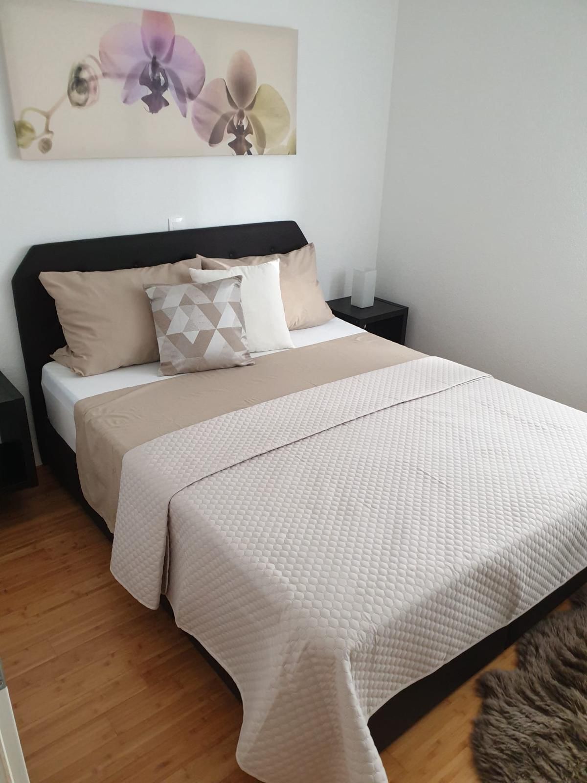 A neatly made bed with a beige quilt, a geometric patterned pillow, and a plain headboard.