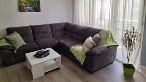 Una sala de estar con un sofá modular de color oscuro, una mesa de centro blanca y una planta en maceta.