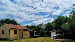 Una propiedad residencial con una casa de piedra, un coche estacionado en la entrada y un cielo despejado.