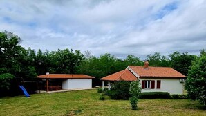 Dos casas pequeñas con tejados rojos, rodeadas de follaje y un cielo nublado.