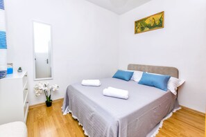 A neatly arranged bedroom with a bed, pillows, a bedside table, a mirror, and a painting on the wall. - Apartment New (Supetar)