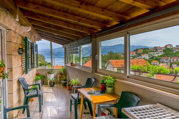 A covered balcony with a view of the sea and mountains, furnished with chairs and tables, and decorated with potted plants. - Apartment New (Supetar)