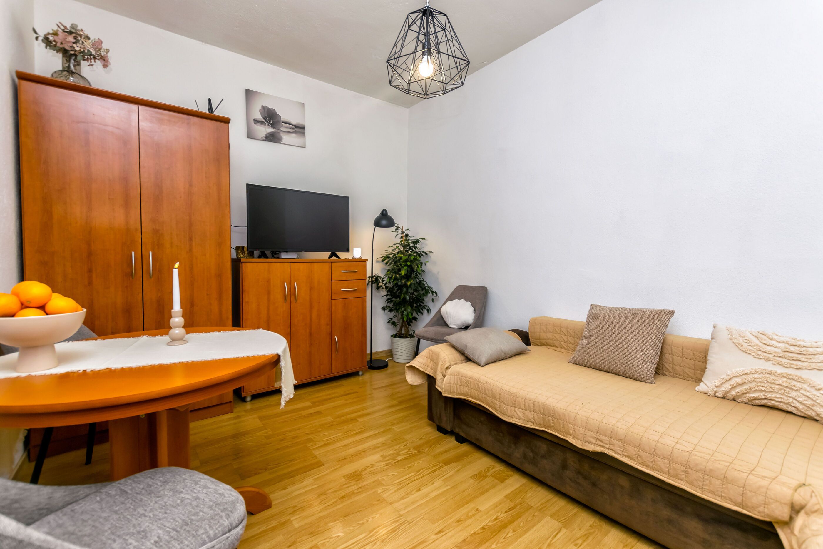 A living room with a wooden cabinet, a TV, a sofa, and a dining table with a bowl of fruit.