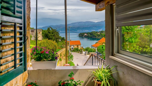 A balcony with a view of a coastal town, stone walls, and potted plants. - Apartment New (Supetar)