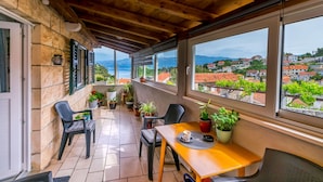 A balcony with a wooden ceiling, stone walls, and a view of a town and mountains. - Apartment New (Supetar)