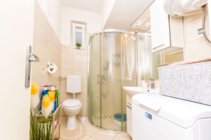 A modern bathroom with a glass shower enclosure, a white toilet, and a sink with a mirror above it. - Apartment New (Supetar)