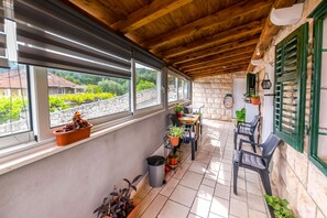 A covered patio with a stone wall, wooden ceiling, and large windows overlooking a vineyard. - Apartment New (Supetar)