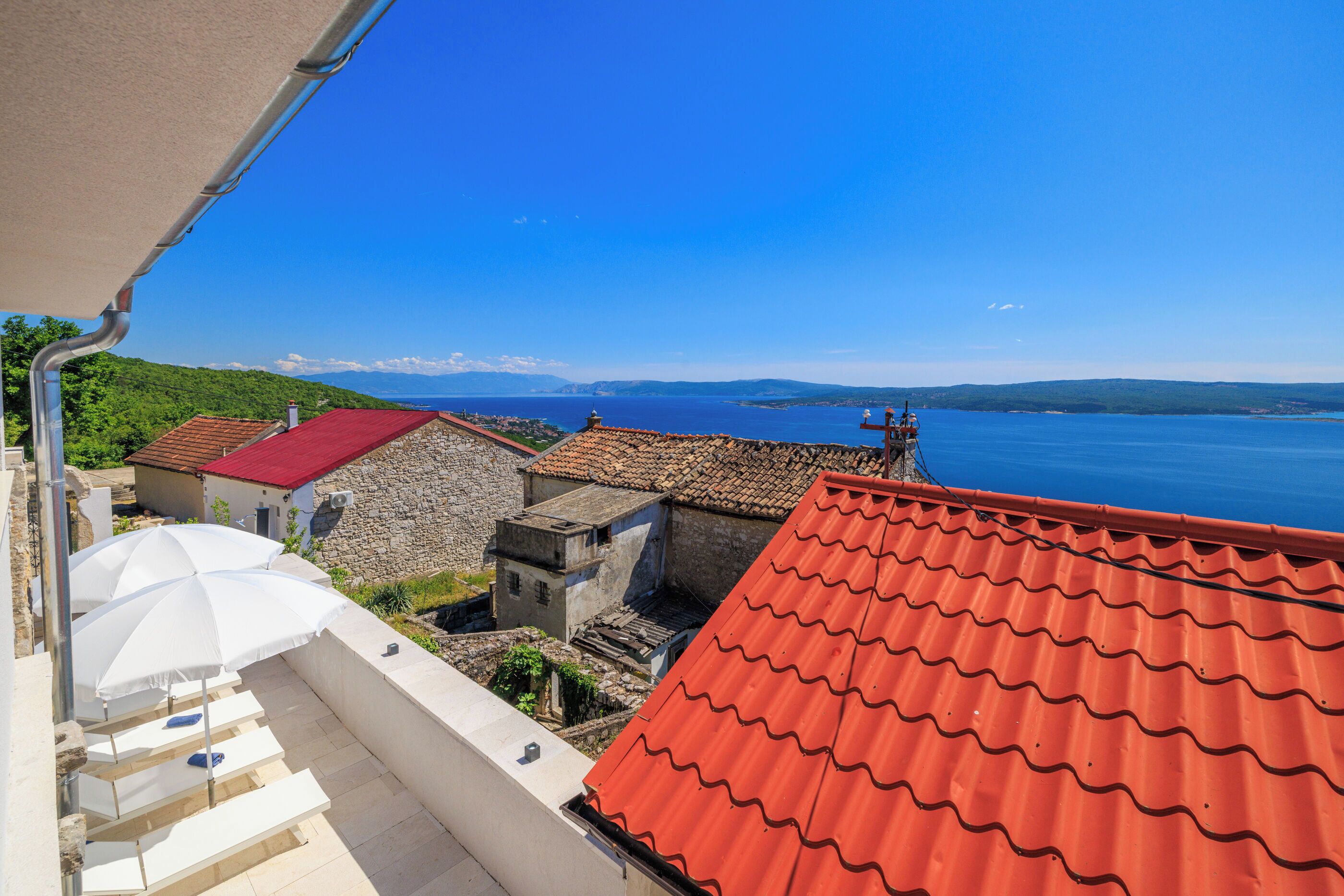Une vue sur la côte, avec un toit recouvert de tuiles rouges, des bâtiments en pierre et un ciel bleu dégagé.