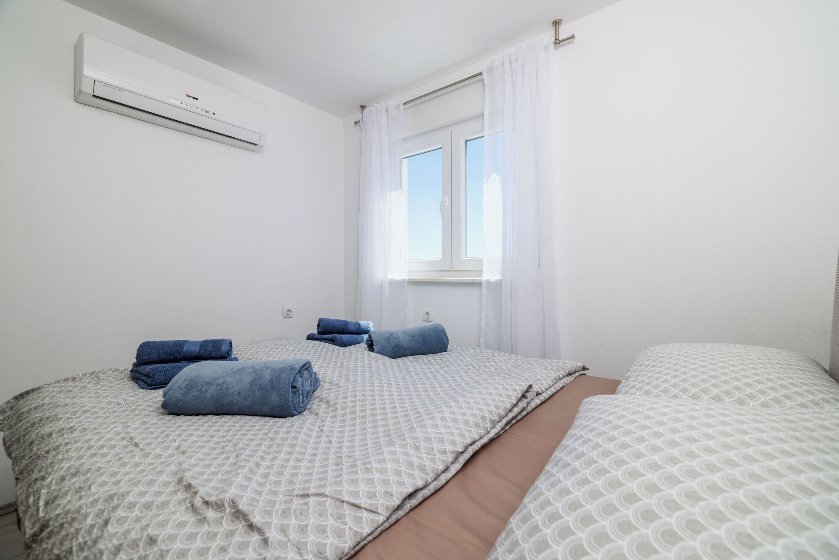 Een hotelkamer met twee bedden, een raam met gordijnen en een airconditioning aan de muur.