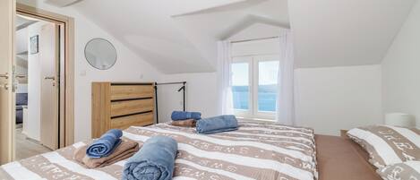 A bedroom with a sloped ceiling, a wooden wardrobe, a bed with striped bedding, and a window with curtains.
