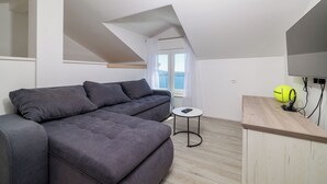 A modern loft apartment with a grey sectional sofa, a small round table, and a wooden desk with a yellow exercise ball. - House Emma (Crikvenica)
