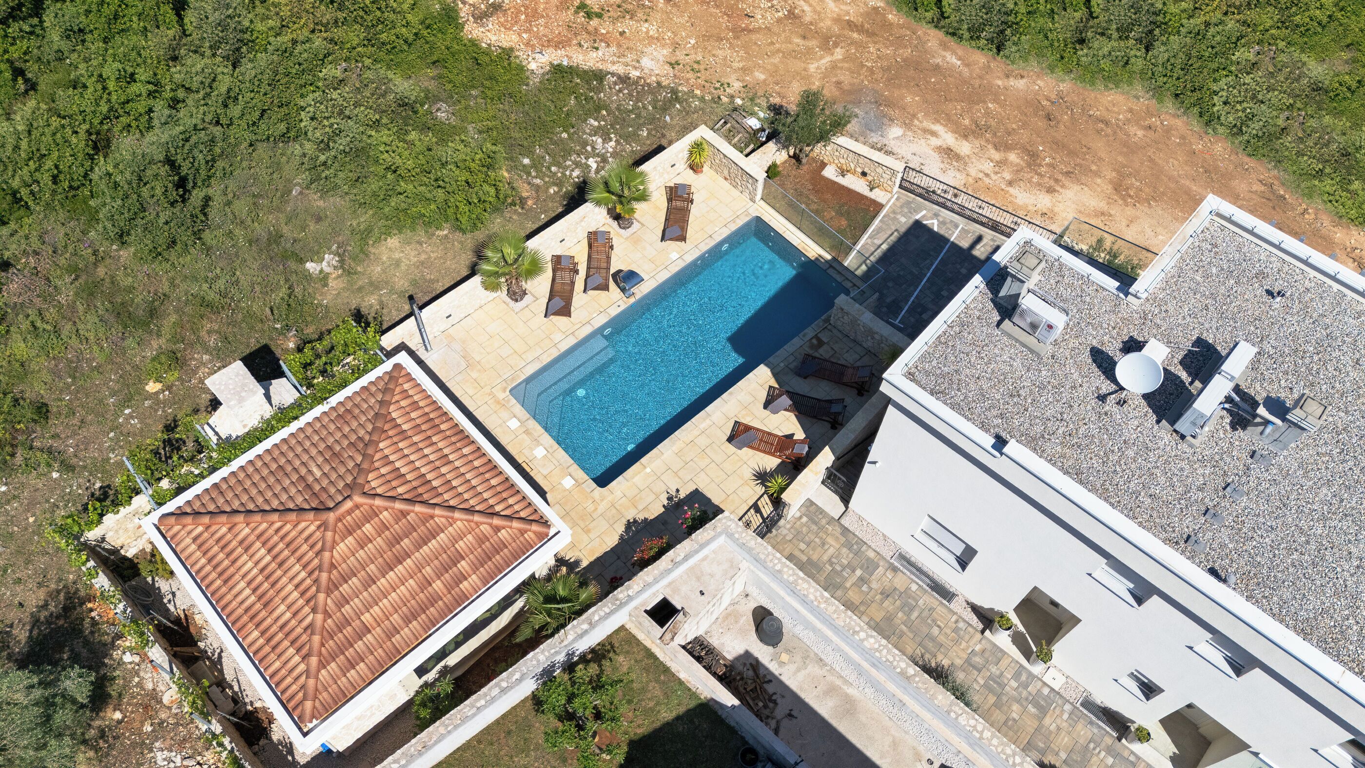 Vue aérienne d’une propriété dotée d’une piscine, d’un patio couvert et d’un bâtiment surmonté d’un toit en tuiles.