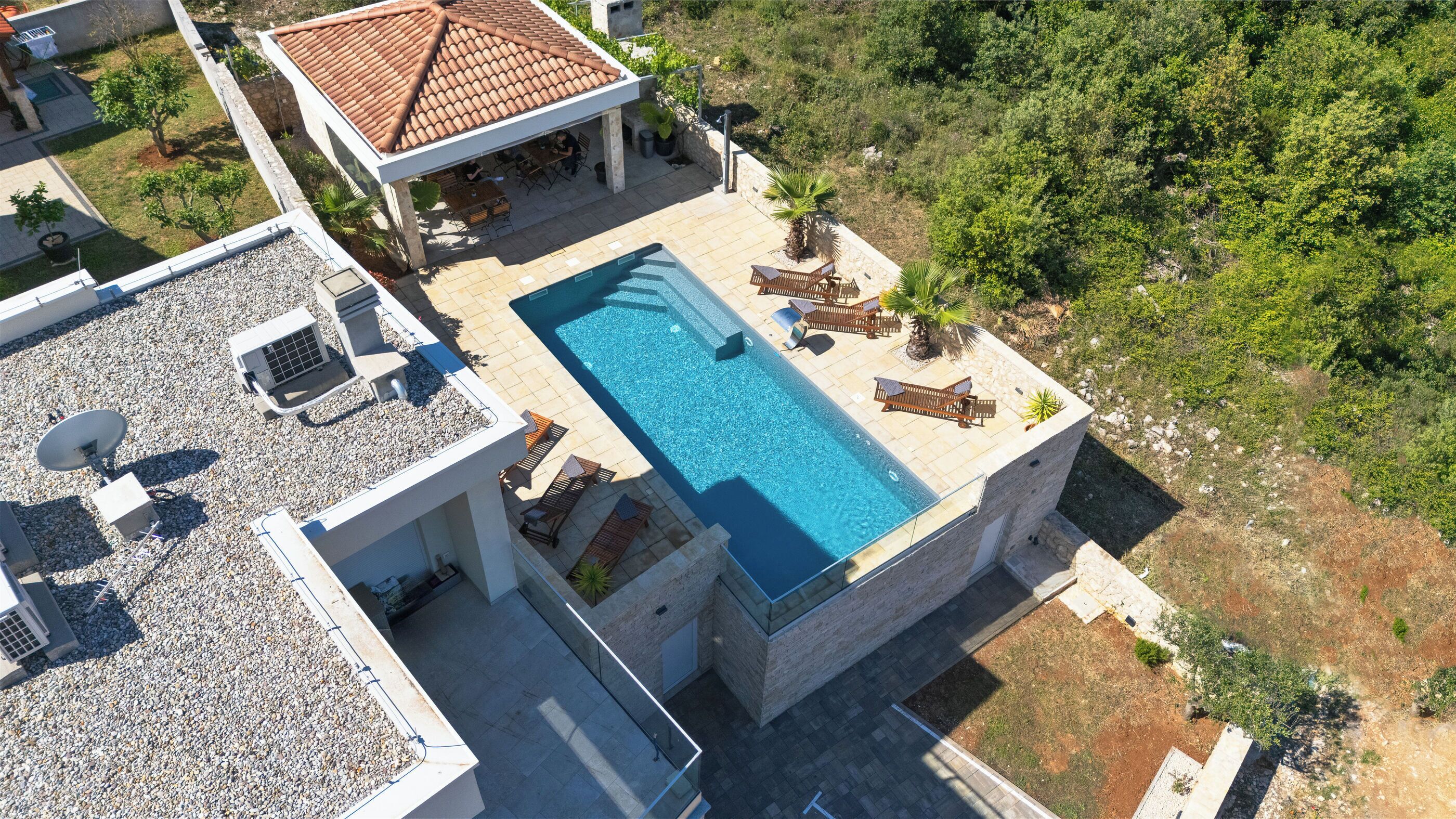 An aerial view of a modern villa with a swimming pool, outdoor seating, and a garden.