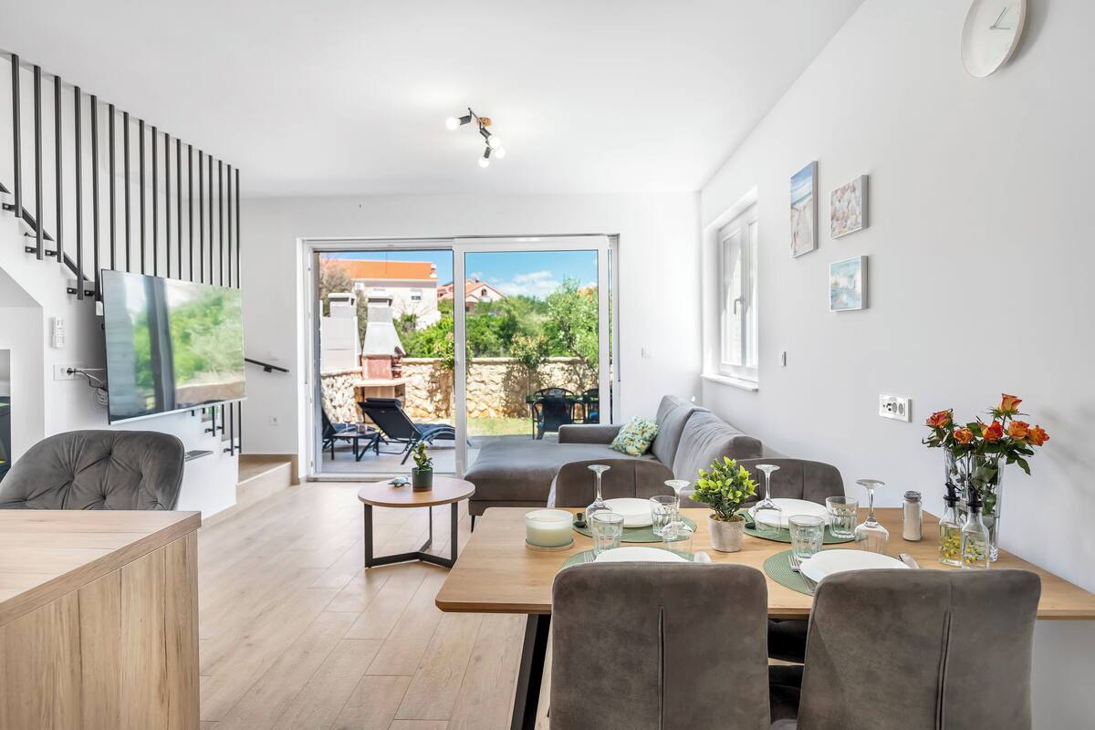 A modern living room with a dining area, a staircase, and a view of the outdoors.