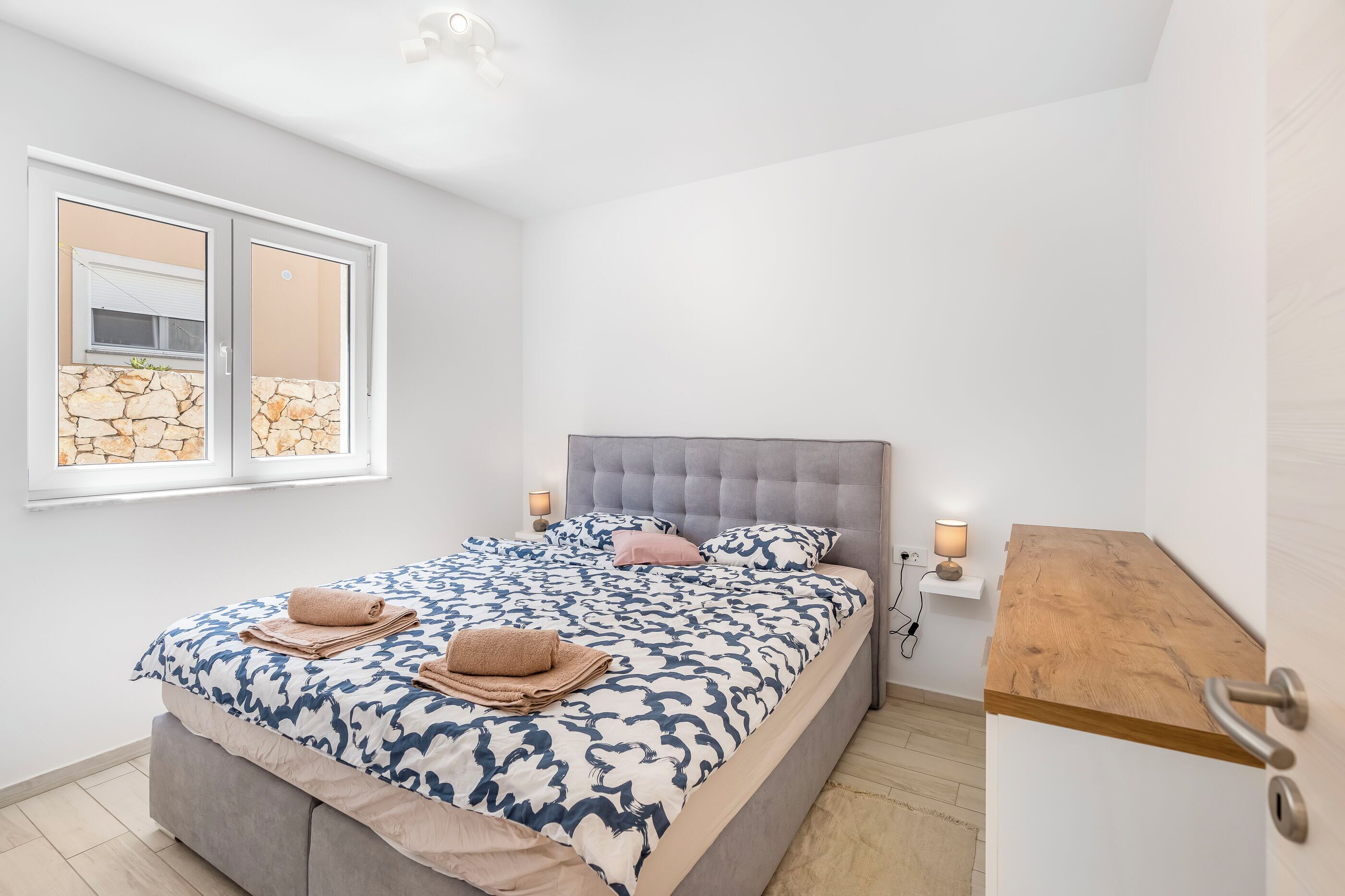 A modern bedroom with a bed, a nightstand, and a wooden shelf.