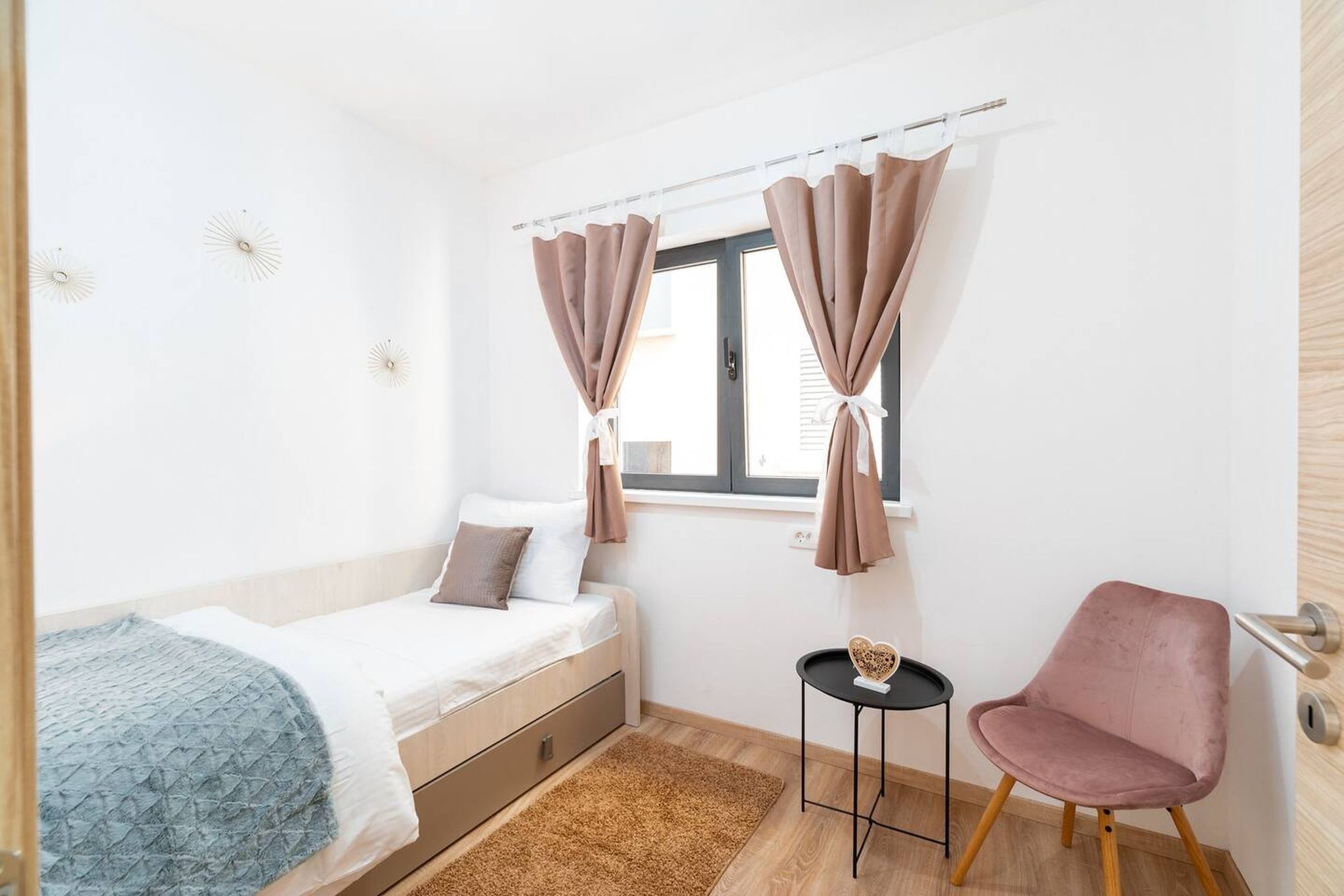 A bedroom with a bed, a small table, a chair, and a window with curtains.